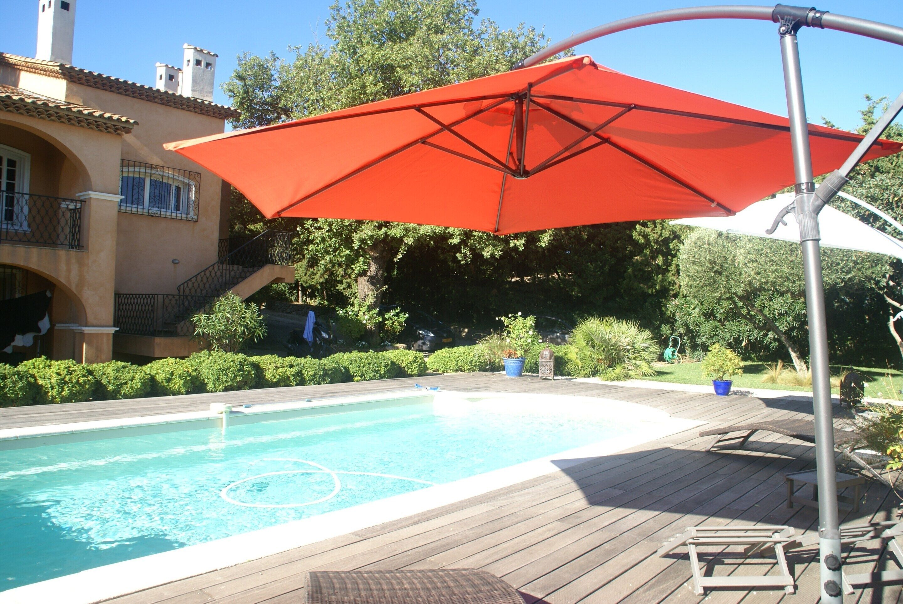 A swimming pool with a wooden deck, an umbrella, and a building with a balcony in the background.