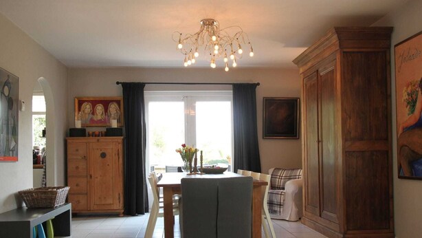 A dining area with a chandelier, wooden cabinets, and a painting on the wall. - Groet Villa Stay With Garden Views (Groet)