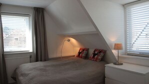 A bedroom with a bed, a bedside lamp, a dresser, and a window with blinds. - Groet Villa Stay With Garden Views (Groet)
