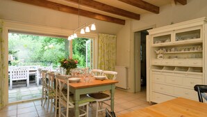 A dining area with a wooden table and chairs, a vase with flowers, and a view of greenery outside. - Secluded Farmhouse in Balkbrug with Hot Tub (Balkbrug)