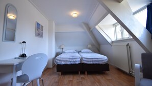 A bedroom with a sloped ceiling, two beds, a desk, and a chair. - Holiday Home Bergen Near Beach & Dunes (Bergen aan Zee)