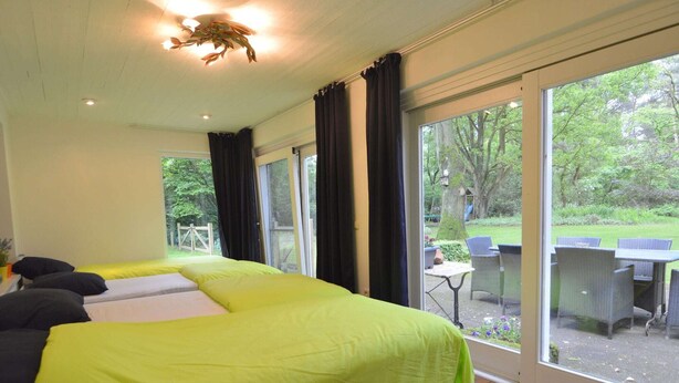 A room with a large bed, a window, and a view of an outdoor area with a table and chairs.