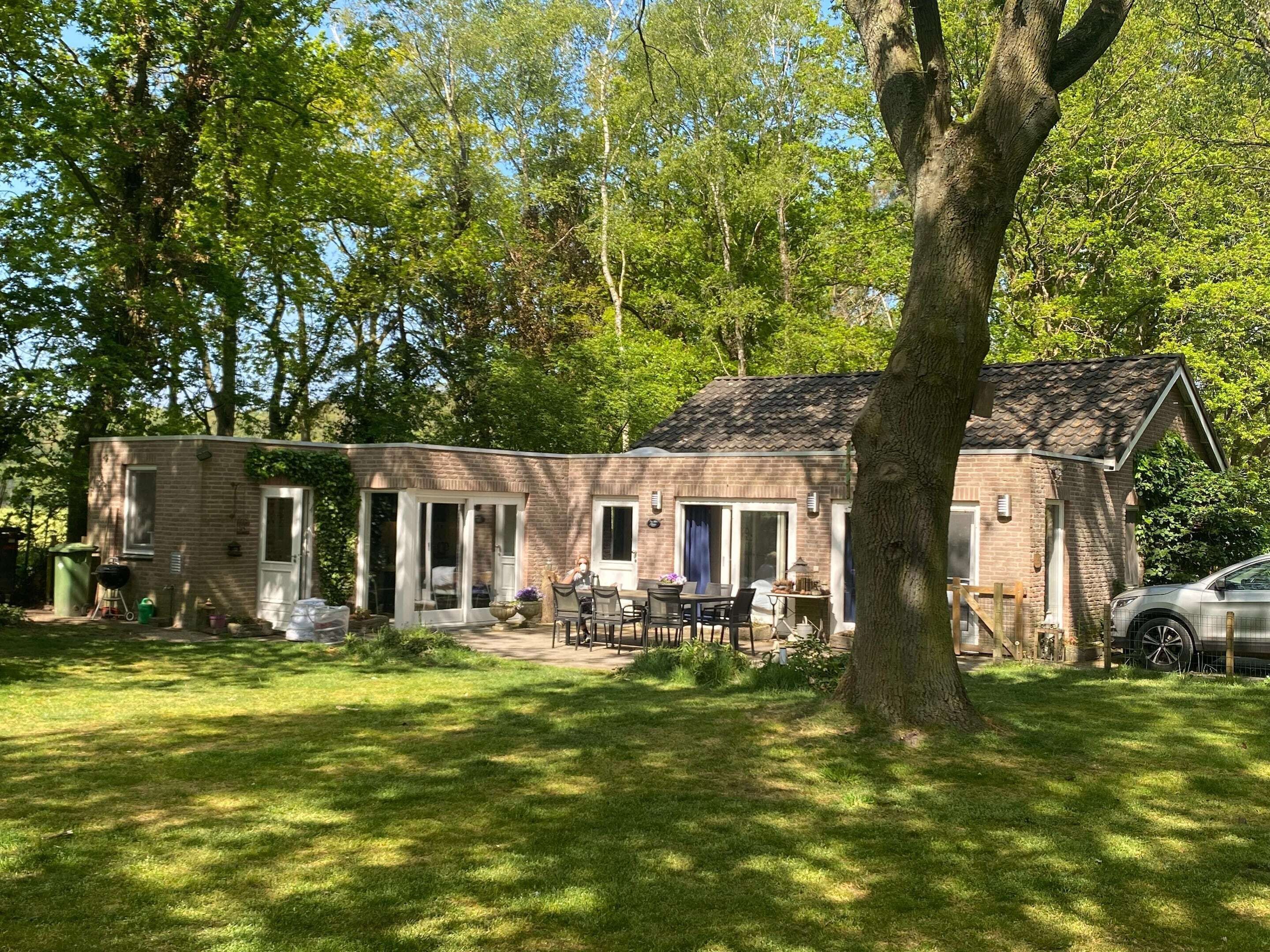 Een tweelaags bakstenen gebouw met een patio en een overdekt terras, en een auto in de buurt geparkeerd.