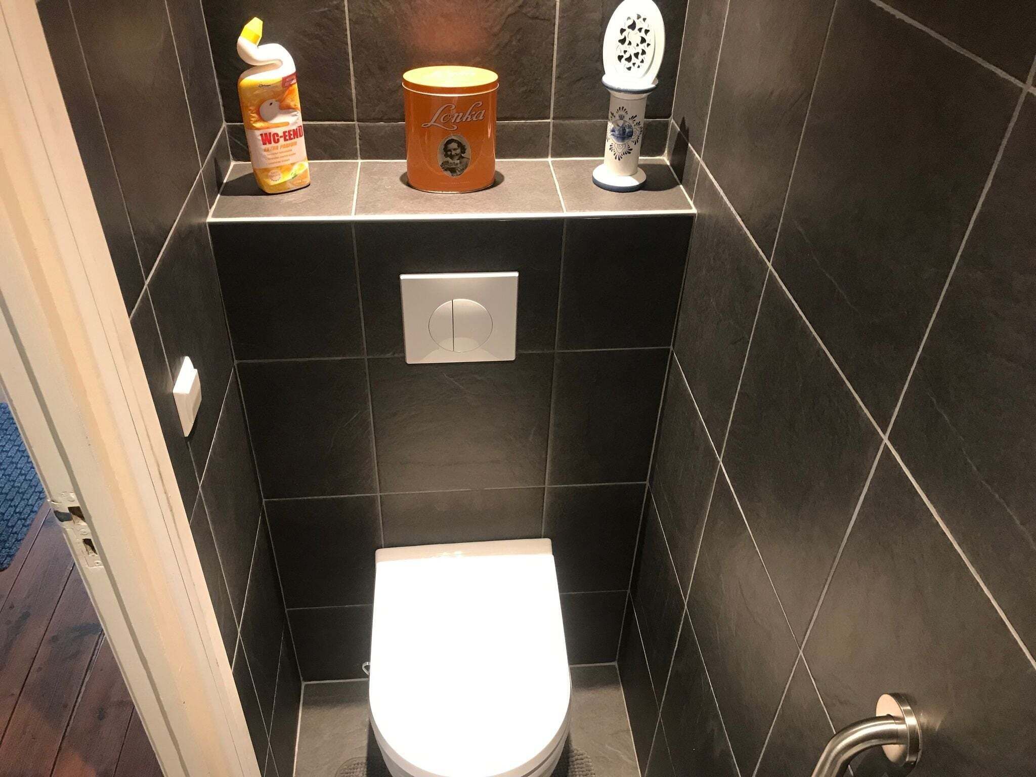 A small, modern bathroom with a toilet, a soap dispenser, and a toilet brush on the wall.