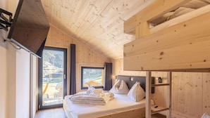 Habitación de cabaña de madera con literas, un ventanal con vistas a una casa y un televisor montado en la pared.