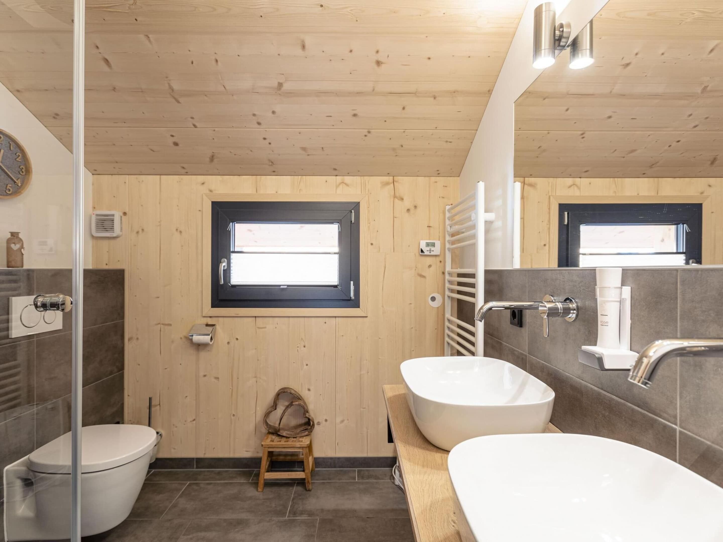 A modern bathroom with a wooden ceiling, a large window, a toilet, a sink, and a shower area.