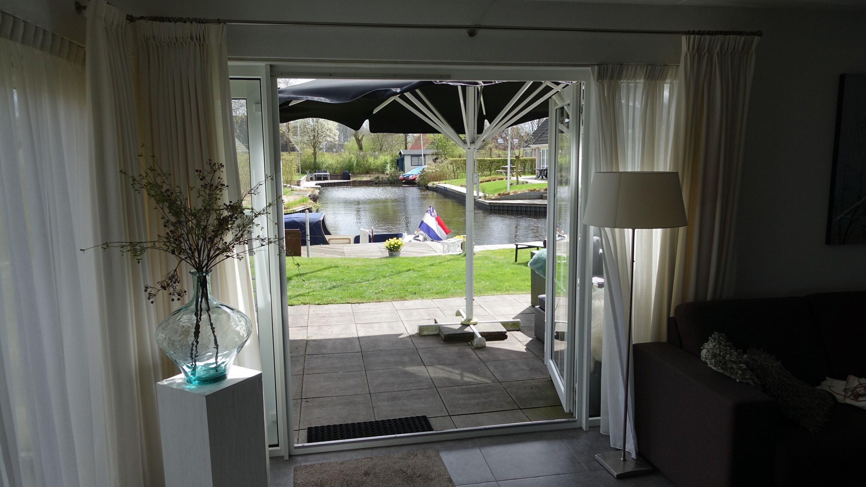 A room with a view of a canal, a glass door, a potted plant, and a lamp.