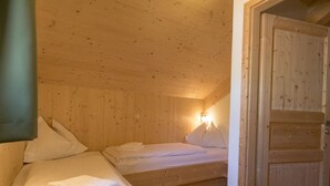 A wooden cabin room with two beds, a door, and a wall-mounted light.