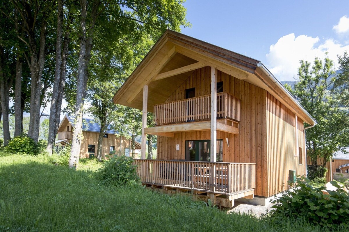 A wooden cabin with a balcony, surrounded by trees and grass.