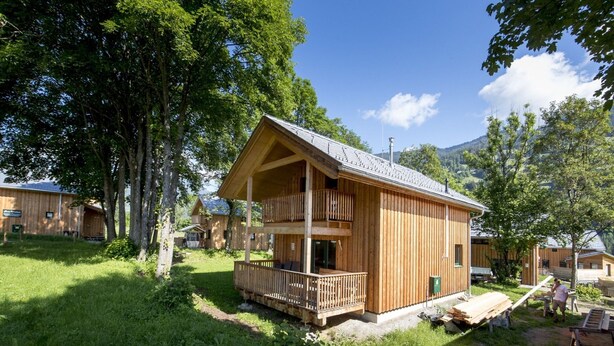 A wooden cabin with a balcony, surrounded by trees and a clear sky.