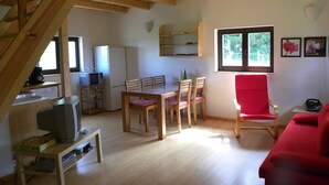 Quarto com mesa de jantar, cadeiras, sofá vermelho, televisão, cozinha com geladeira e janela com vista para áreas verdes.
