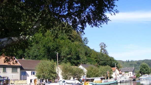 Um rio calmo com barcos atracados na margem, rodeado por edifícios residenciais e vegetação exuberante.