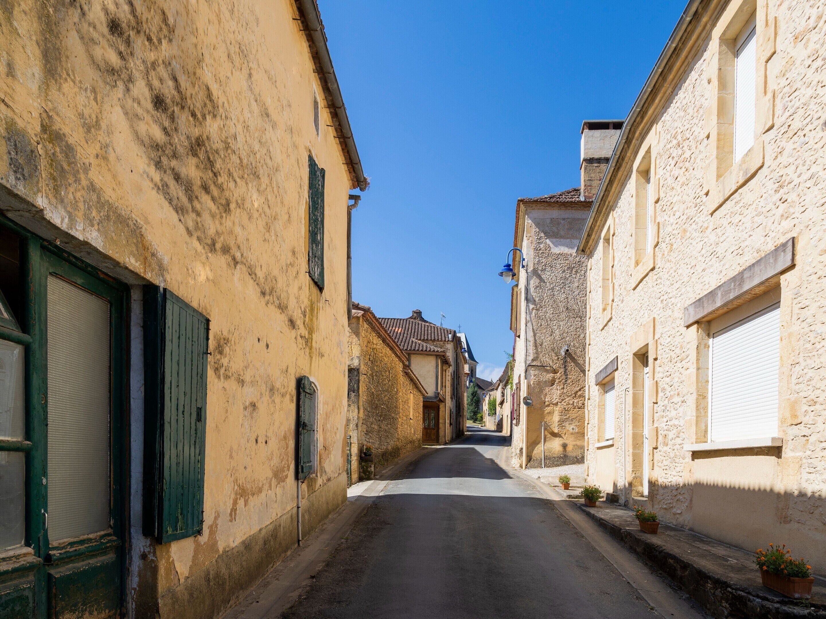 Une rue étroite bordée de vieux bâtiments aux fenêtres et aux portes fermées par des volets.