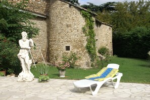 Ein Steinhaus mit einer Statue, einem weißen Liegestuhl und Topfpflanzen.