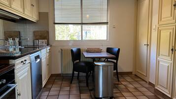 A kitchen with a dining table, chairs, a trash bin, and cabinets.