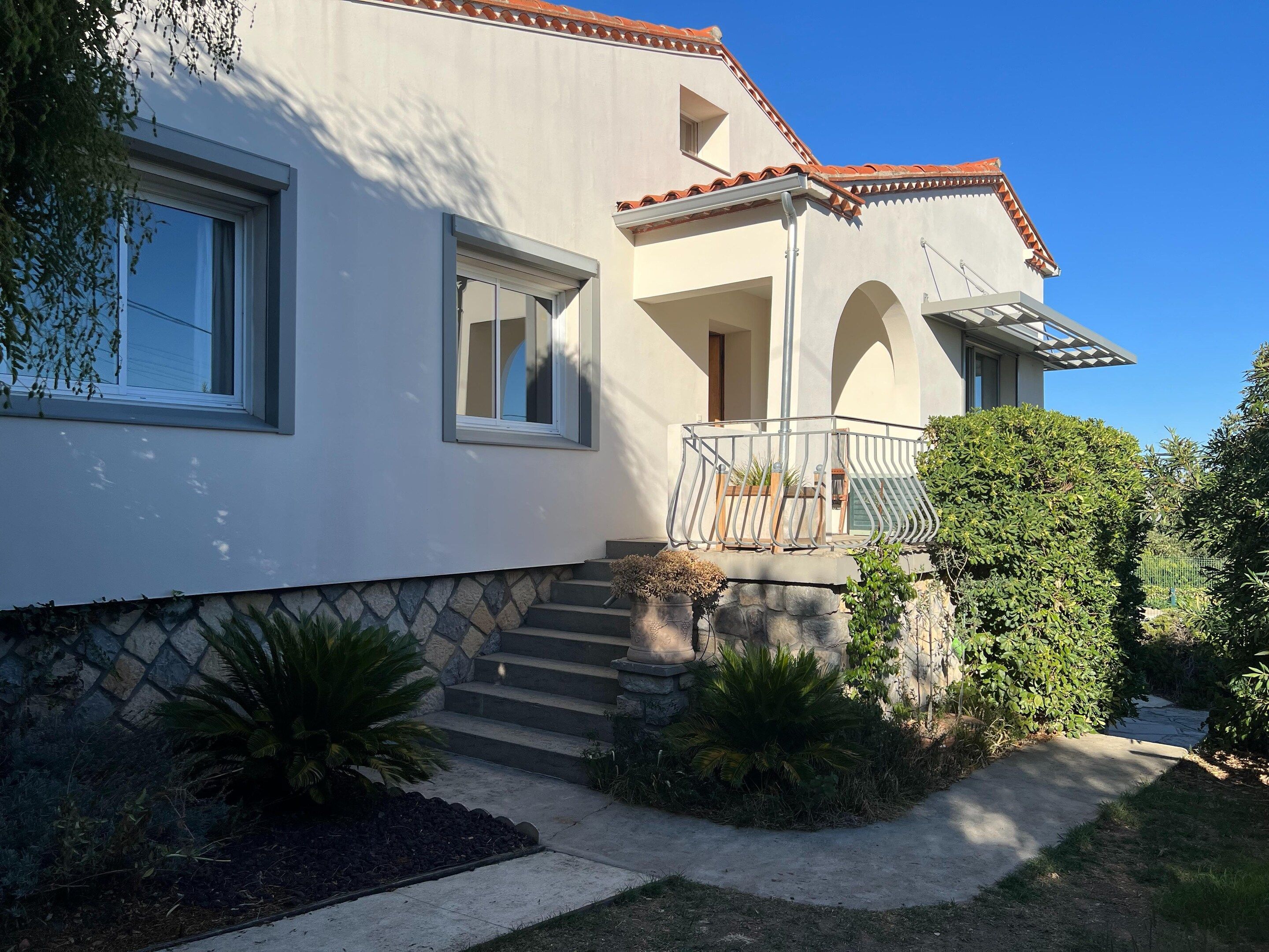 A two-story house with a balcony, a stone staircase, and a well-maintained garden.