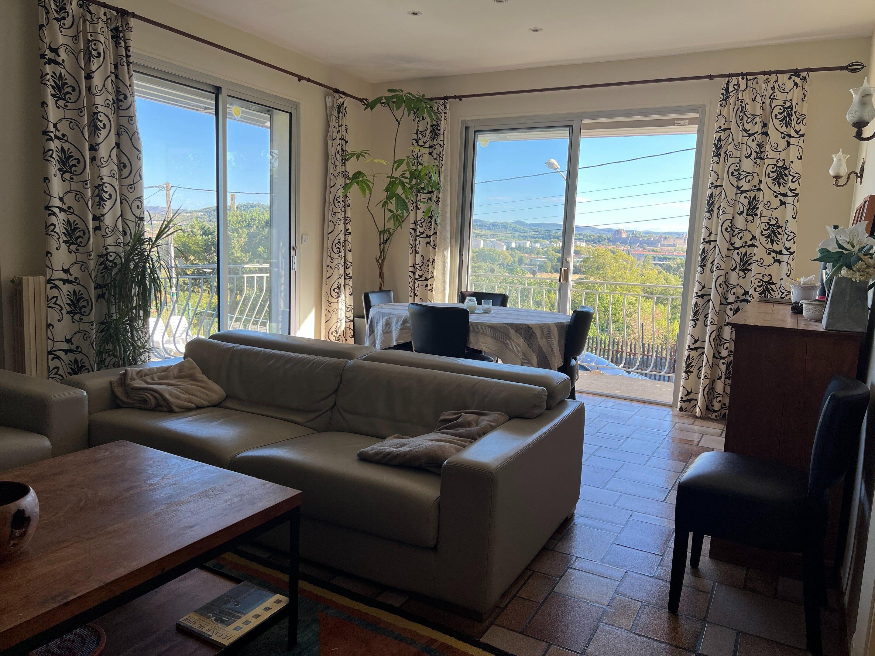 A living room with a sofa, a dining table, and a balcony with a view.