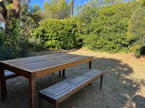Una mesa de picnic de madera con bancos en un jardín rodeado de abundante follaje.