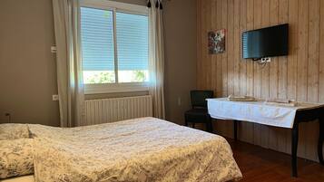 A room with a bed, a table, a chair, a television, and a window with curtains.