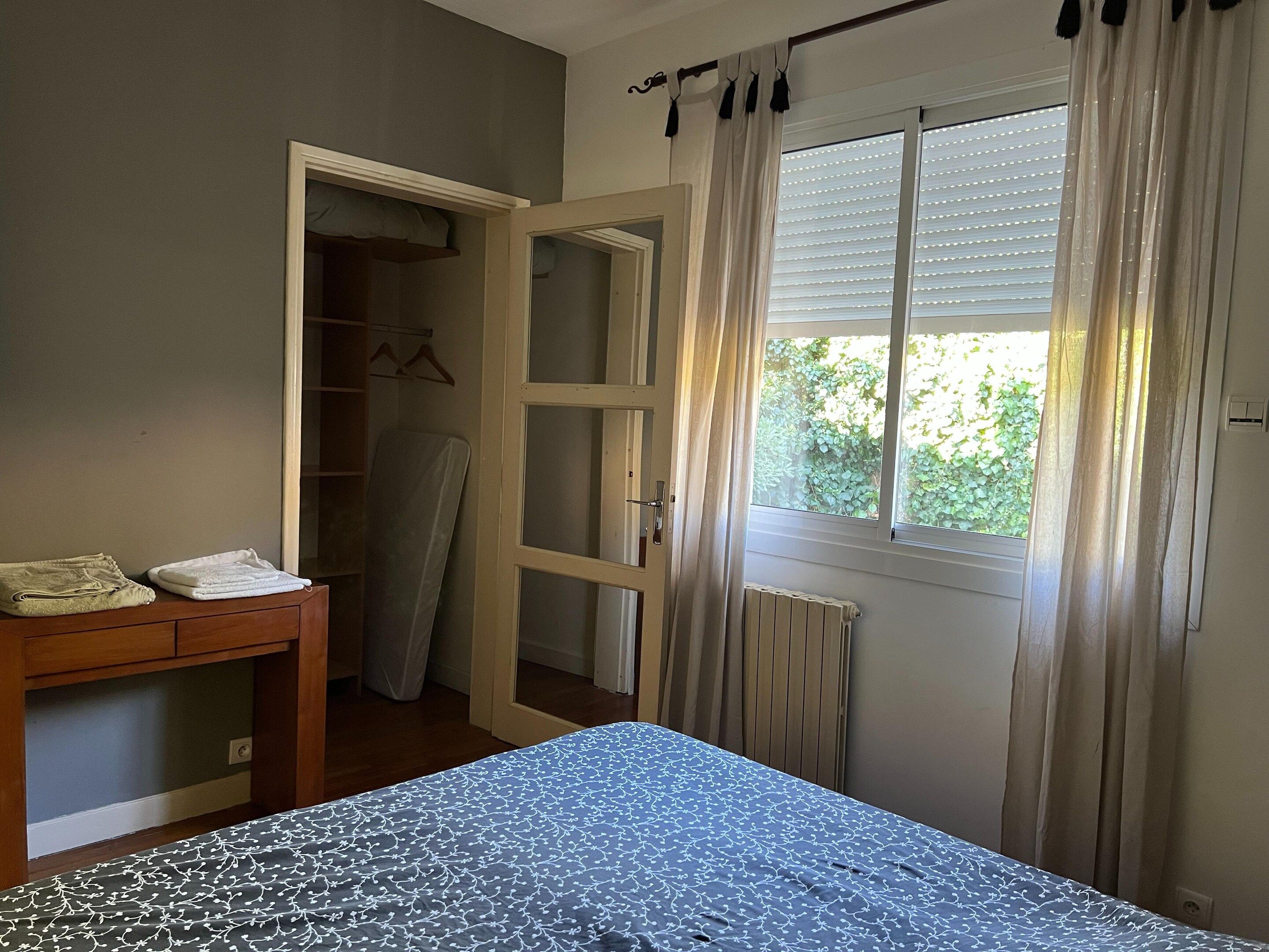 A bedroom with a bed, a bedside table, a wardrobe, and a window with curtains.