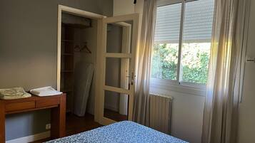 A bedroom with a bed, a bedside table, a wardrobe, and a window with curtains.
