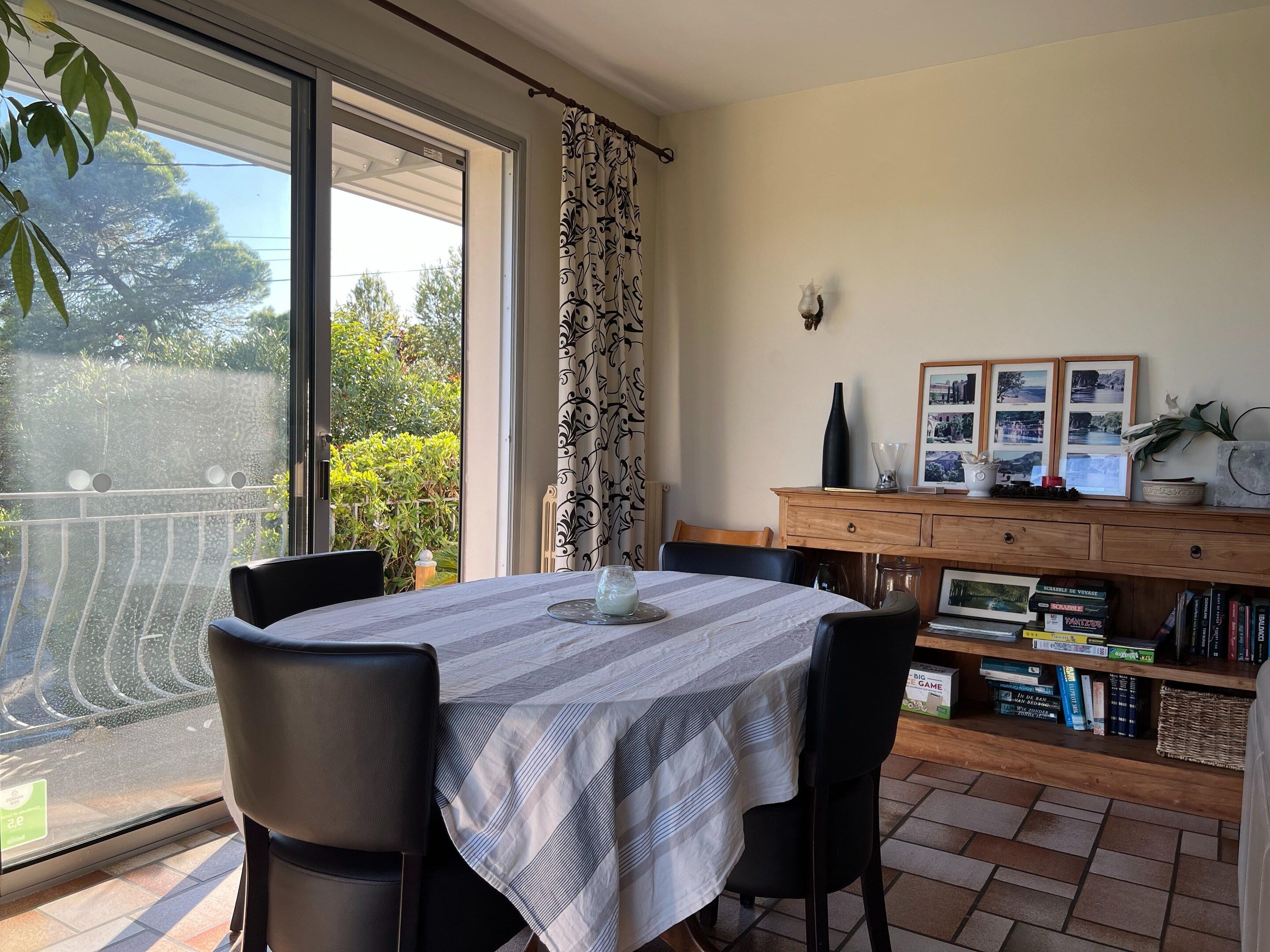 A dining area with a table, chairs, a bookshelf, and a view through a glass door.