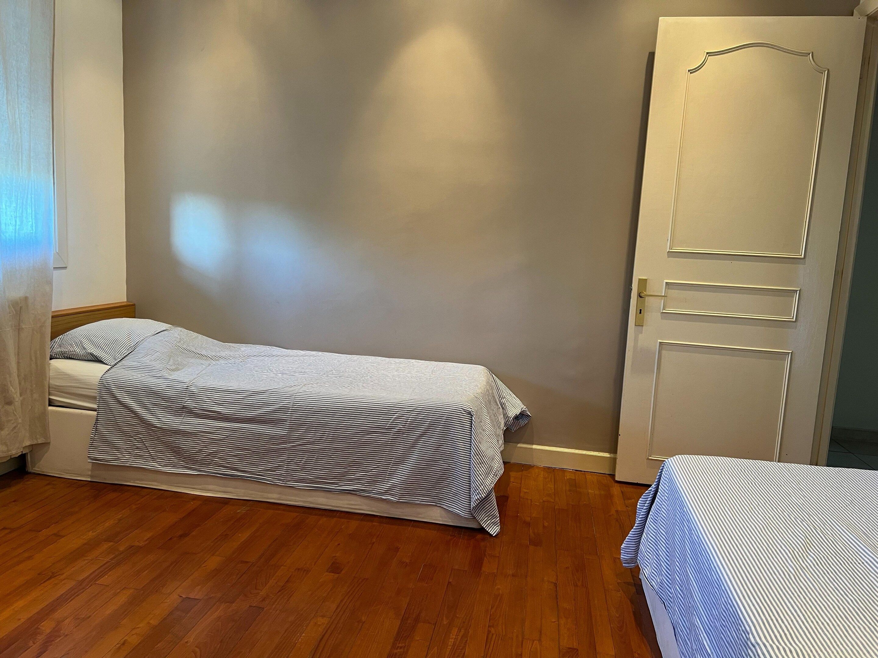 A single bed with a striped bedspread in a room with wooden flooring and a plain wall.