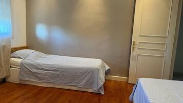 A single bed with a striped bedspread in a room with wooden flooring and a plain wall.