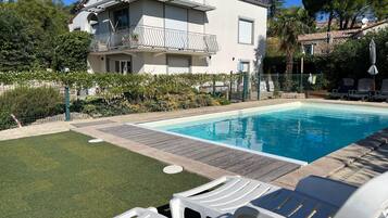 A swimming pool with lounge chairs, a fenced garden, and a two-story building with a balcony.