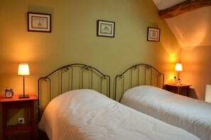 Een kamer met twee bedden, een houten hoofdbord, een nachtkastje met een lamp en lijstjes met foto's aan de muur.