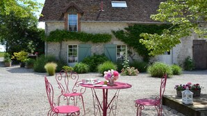 A stone house with a gravel courtyard, red metal chairs, a round table, and potted plants. - Holiday Home in Chilleurs Near Chateau (Chilleurs-aux-Bois)