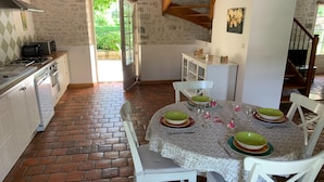 A kitchen with a brick floor, white cabinets, and a dining table set with green bowls and wine glasses. - Holiday Home in Chilleurs Near Chateau (Chilleurs-aux-Bois)