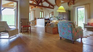 Un amplio salón con vigas de madera, una zona de comedor y una cocina al fondo.