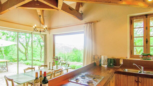 Una cocina con una isla de madera, un comedor con mesa y sillas, y vistas a zonas verdes al exterior.