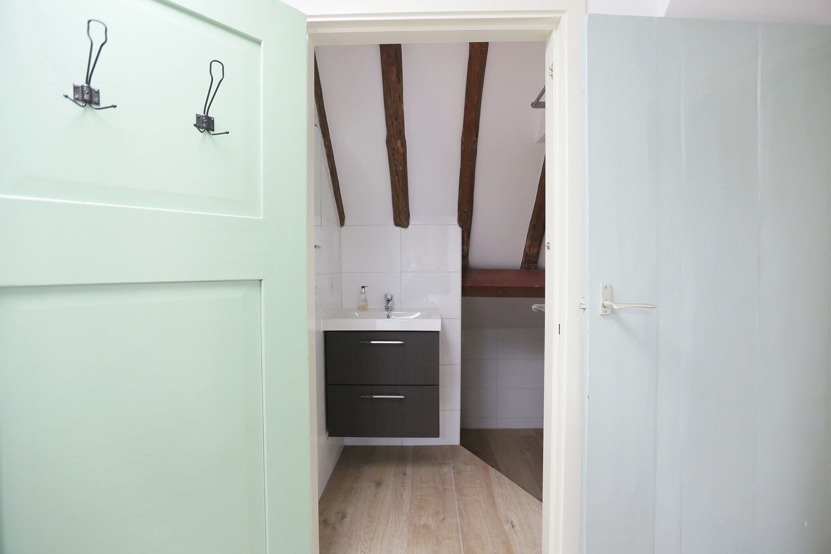 Une salle de bain avec un lavabo blanc, un meuble sombre et des poutres en bois au plafond.