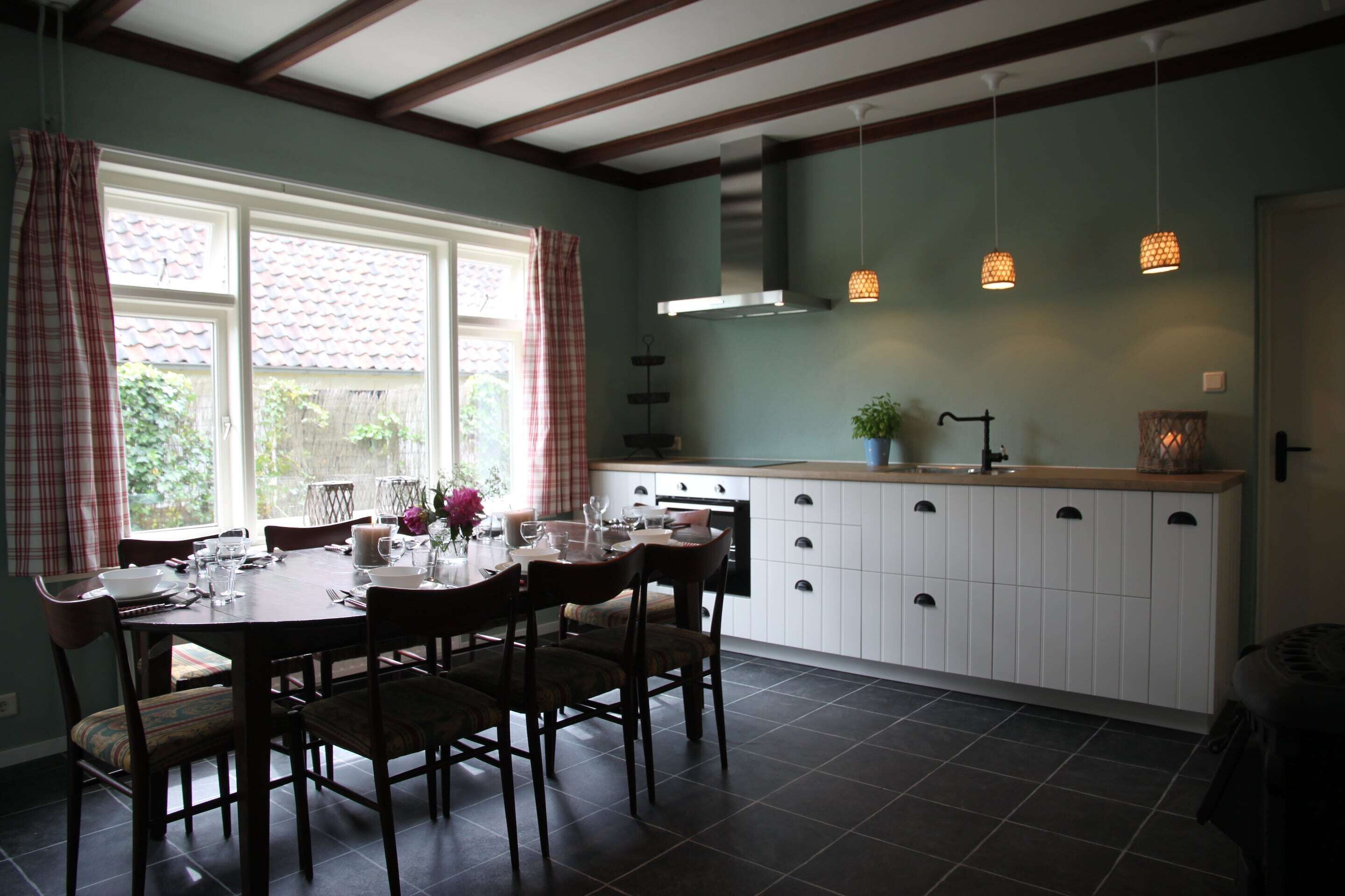 A dining area with a table set for four, a kitchen with white cabinets, and a window with curtains.