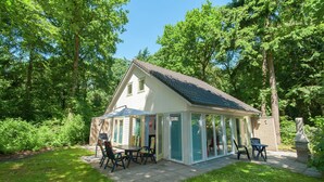 A house with a patio, a covered outdoor seating area, and a statue in the garden. - Superb Villa in the Woods of Gaasterland With Wifi and Fireplace (Oudemirdum)