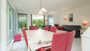 A spacious room with a large dining table, red chairs, a black leather sofa, and a TV. - Superb Villa in the Woods of Gaasterland With Wifi and Fireplace (Oudemirdum)