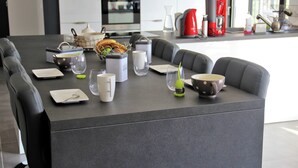 Una cocina moderna con una mesa de comedor preparada para cuatro personas, equipada con diferentes electrodomésticos y utensilios de cocina.