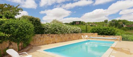 A rectangular swimming pool with a stone wall and a white chair.