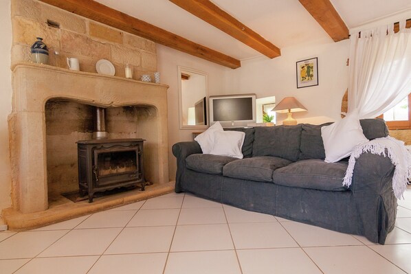 A living room with a stone fireplace, a sofa, a television, and a lamp. - Peaceful Stay With Pool (Badefols-d'Ans)