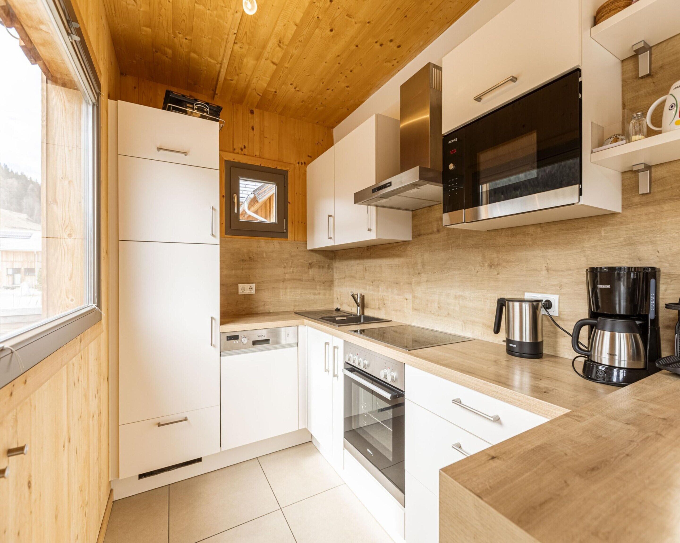 Eine moderne Küche mit Holzboden, weißen Schränken, Edelstahlgeräten und einem Fenster.