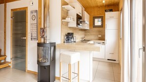 A modern kitchen with a central wood stove, white cabinetry, and a small island with stools. - Lovely Chalet With Whirlpool (Murau)