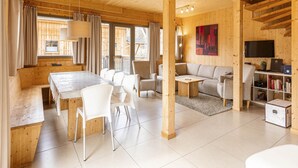A spacious living area with a wooden ceiling, a dining table with chairs, a sofa, a TV, and a bookshelf. - Lovely Chalet With Whirlpool (Murau)
