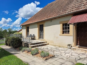 Une maison avec un toit en tuiles, une terrasse en pierre et un petit jardin.