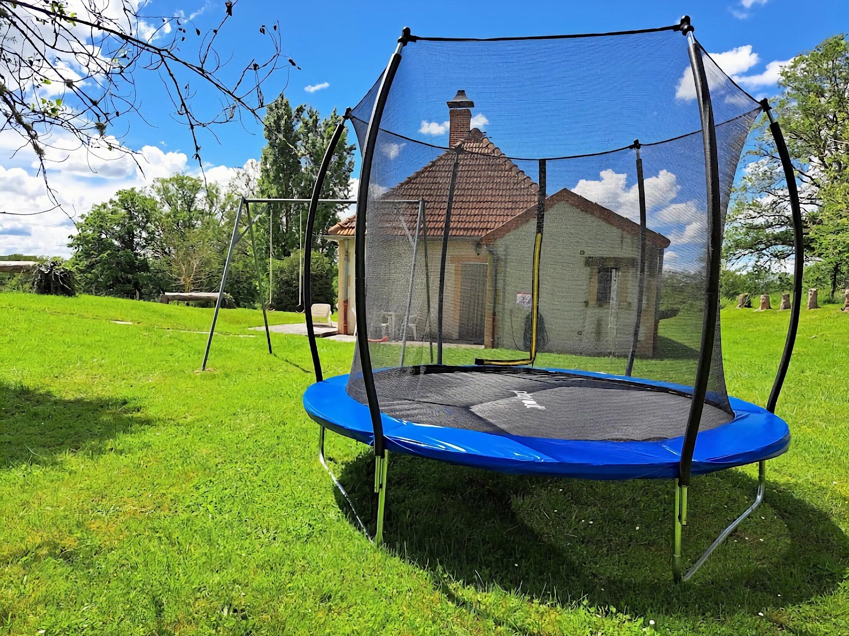 A trampoline with a safety net in a grassy yard with a house in the background.