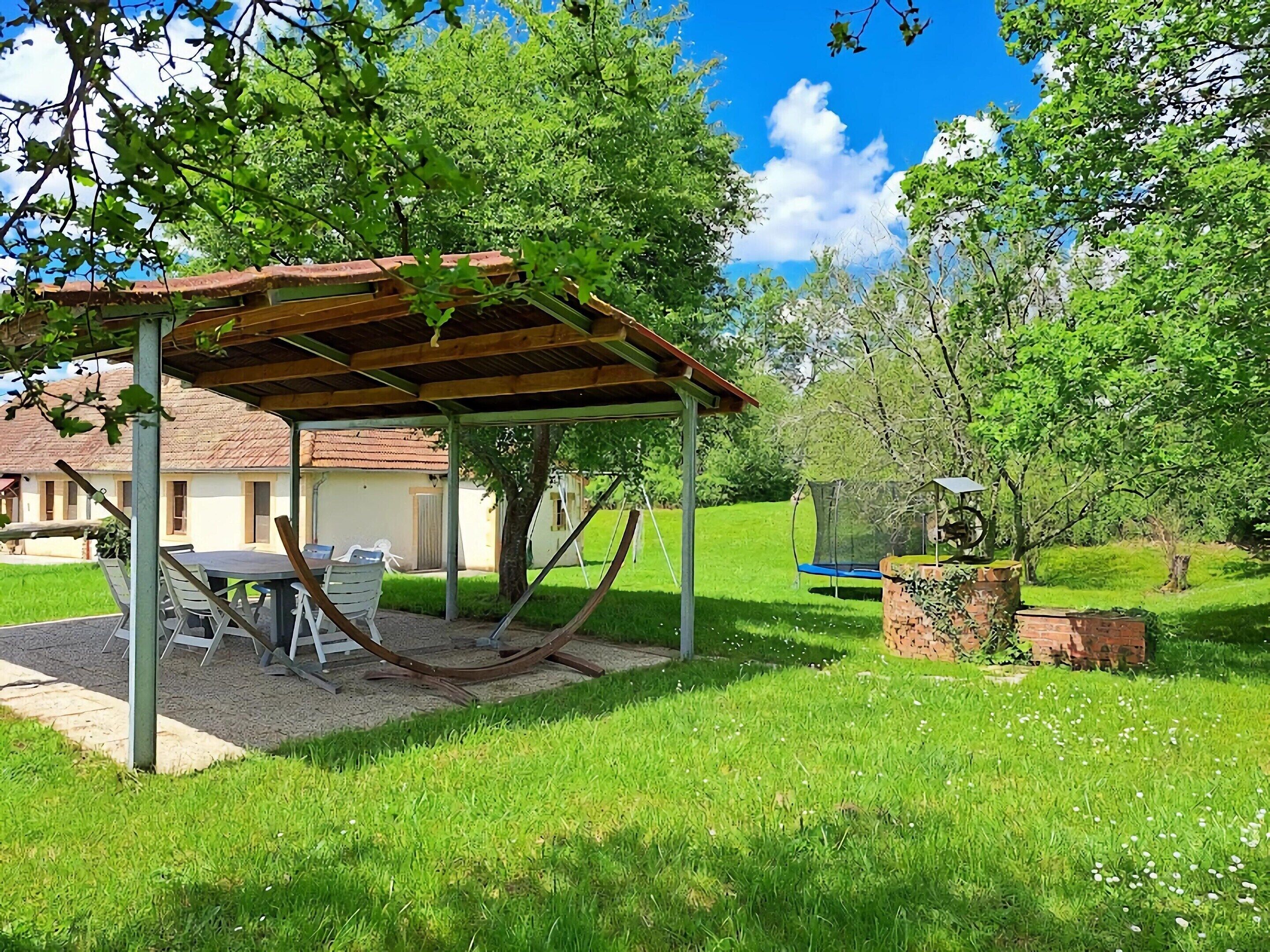 A covered outdoor seating area with a table and chairs, a hammock, and a swing set.