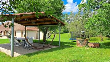 A covered outdoor seating area with a table and chairs, a hammock, and a swing set.