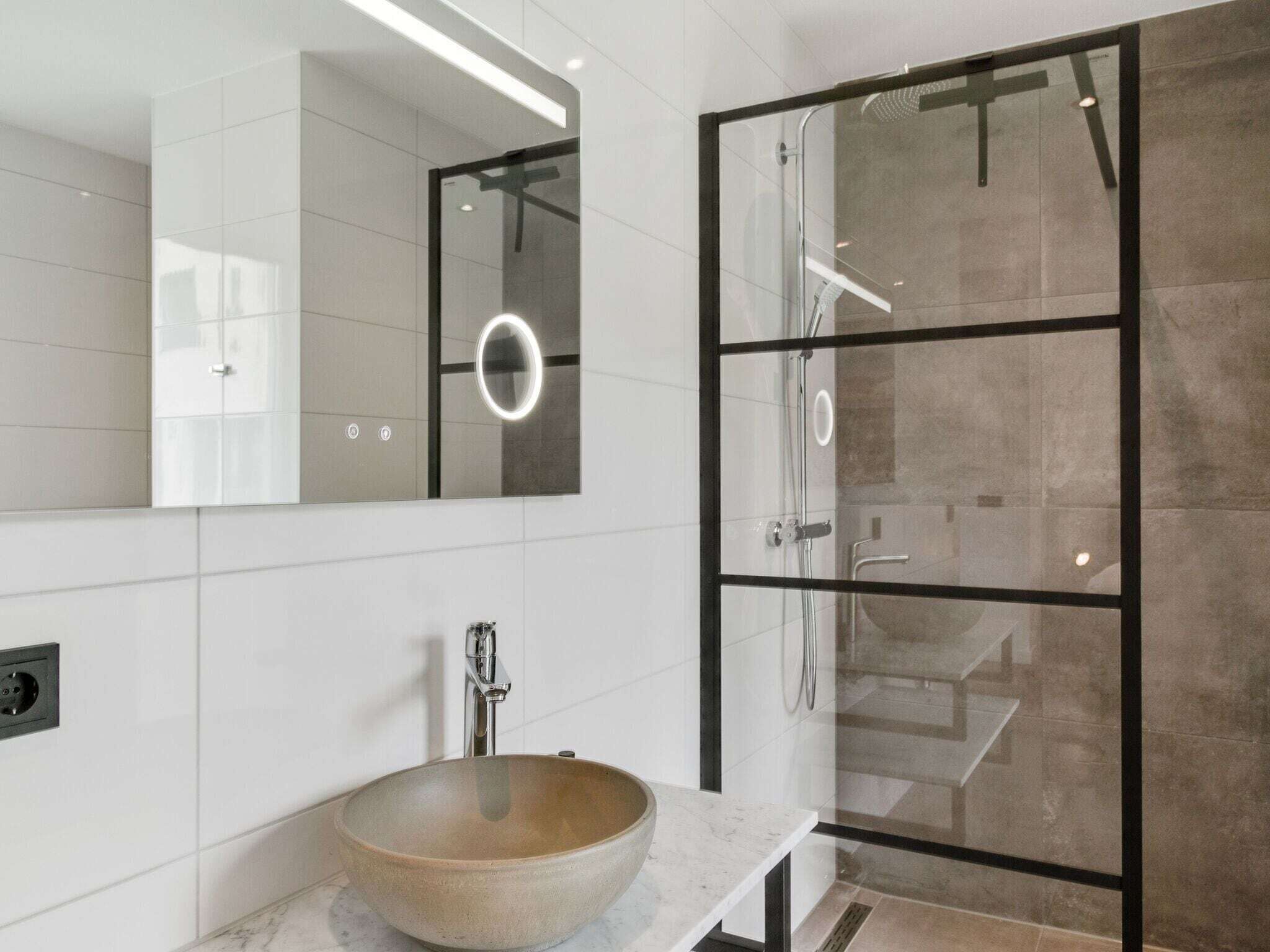 Un baño moderno con un espejo grande, un lavabo redondo y una ducha con mampara de vidrio.