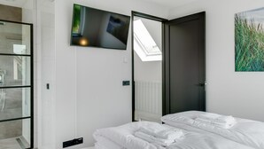 A modern hotel room with a bed, a TV mounted on the wall, a skylight, and a glass shower enclosure. - Bungalow in Texel Near National Park Dunes (De Koog)